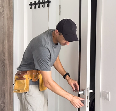 Man installing a door with a tool belt and cap.