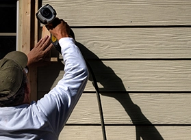 Person using power tool on exterior siding under sunlight.