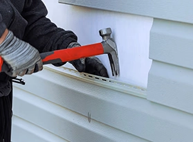 Person using a hammer on exterior house siding.