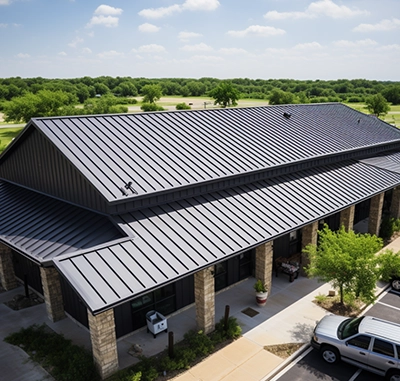 Large metal-roofed building surrounded by greenery on a sunny day.