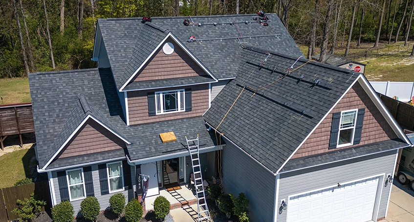 House with new gray roofing and workers on site, ladder leaning against facade.