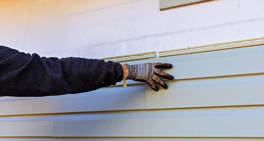 Hand wearing gloves adjusting light blue siding on a wall.